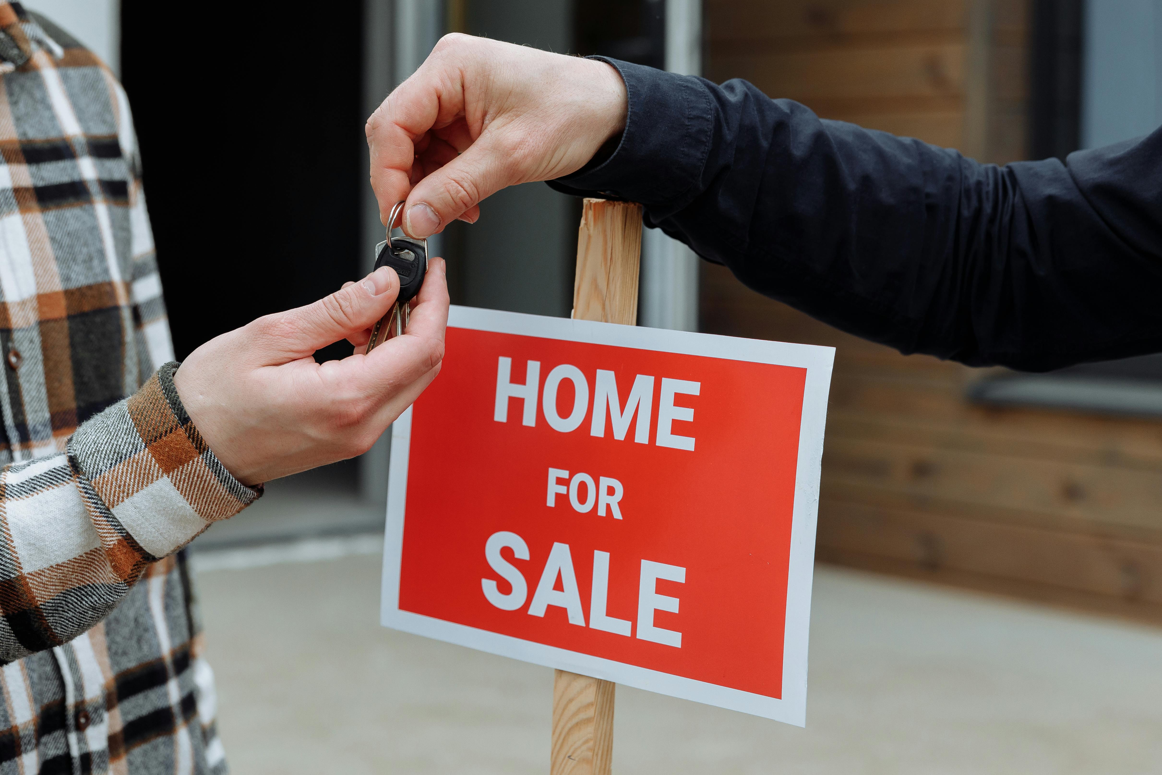 Home for sale sign with people exchanging keys