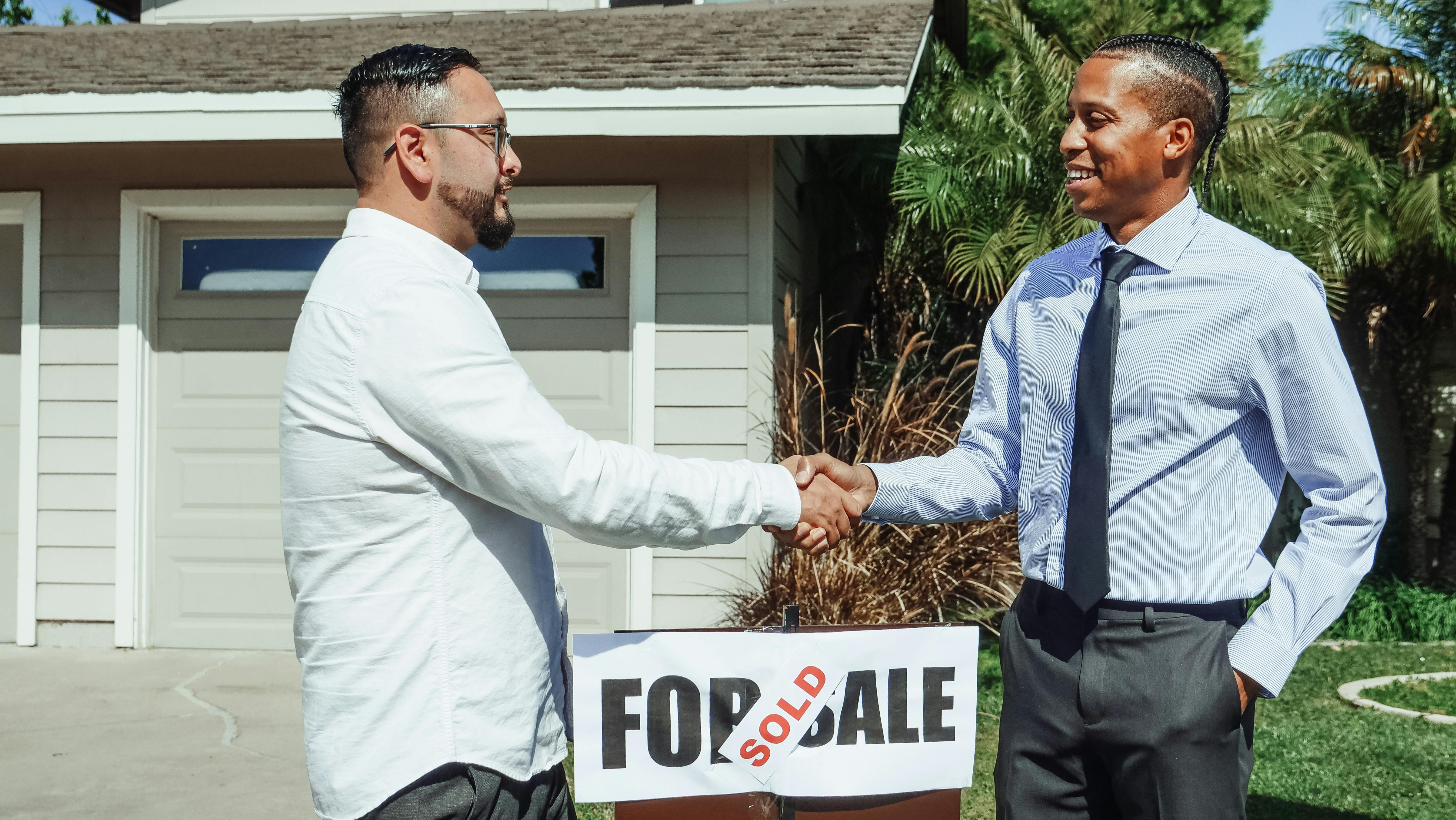 Two men shaking hands in front of sold sign